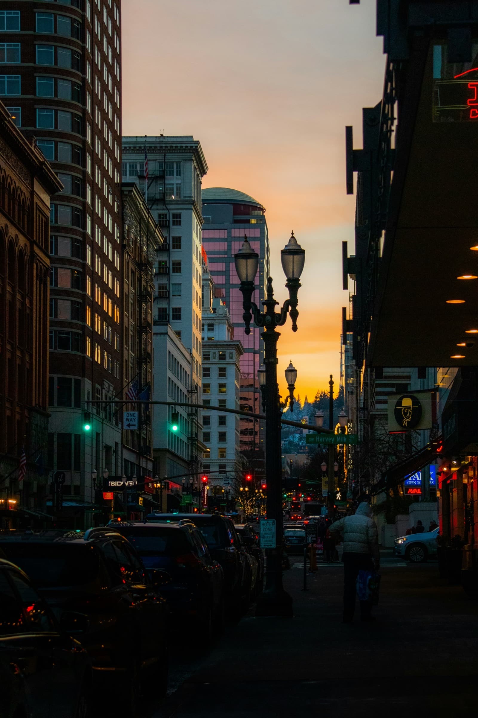 A Portland street at dusk, string lights and lamp posts lit against the sunset